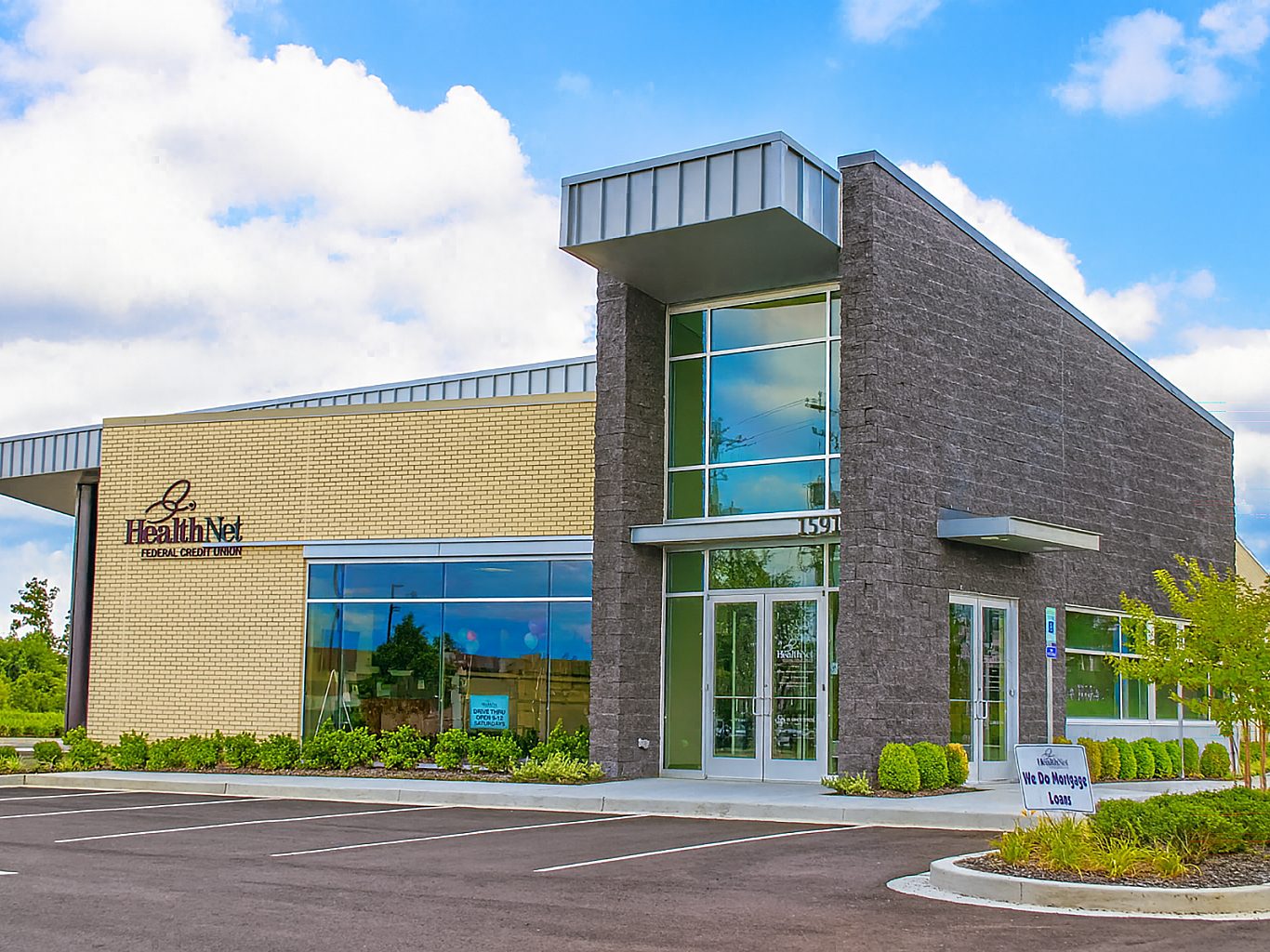 The exterior of an office building for a credit union with wood paneling on one wall and large windows on another portion.