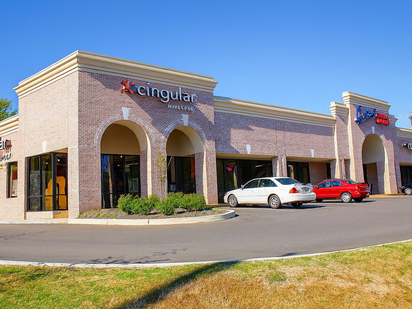 The exterior of a shopping center with two cars in the parking lot
