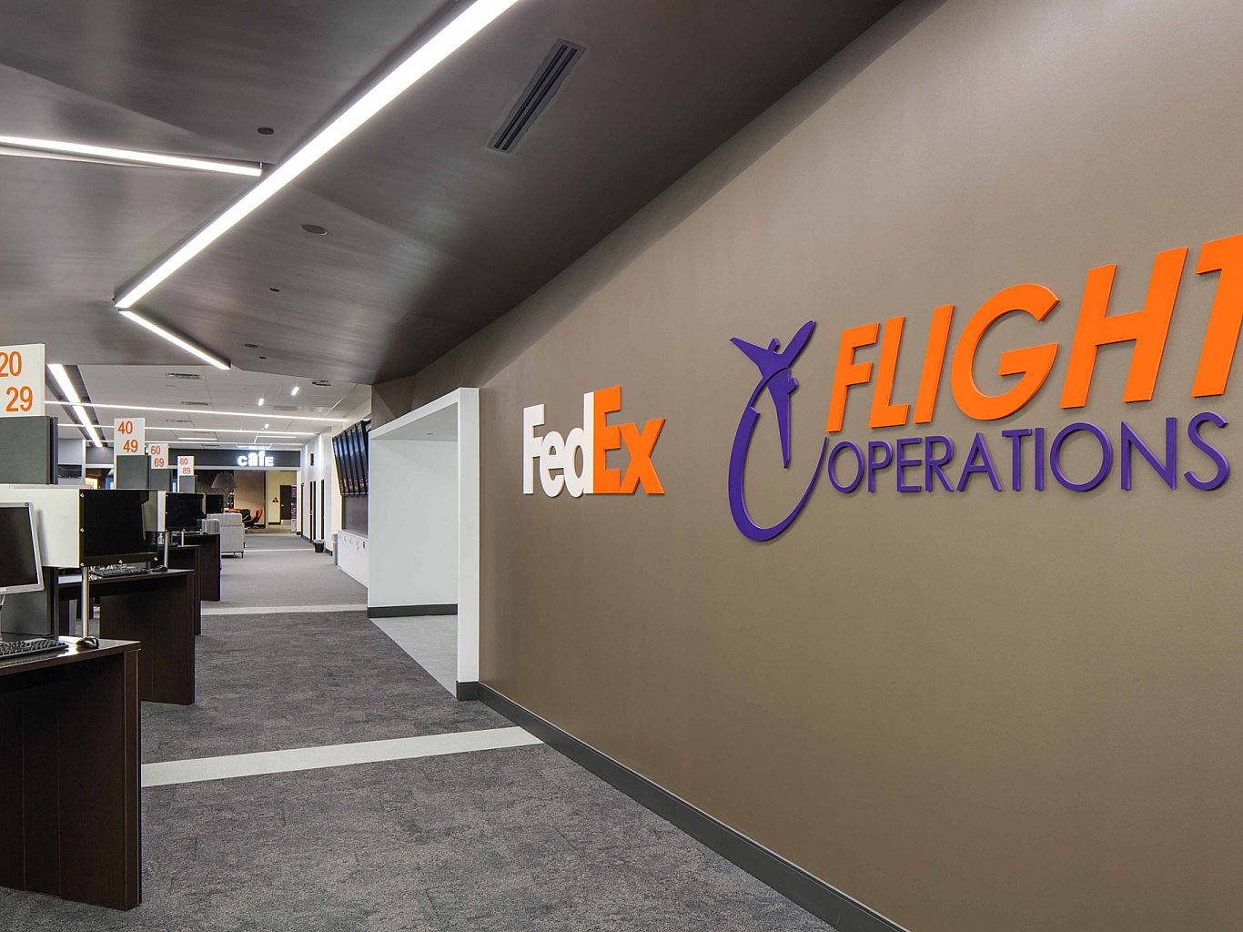 A hallway in a FedEx office building with desks with computers on them lining the left side.
