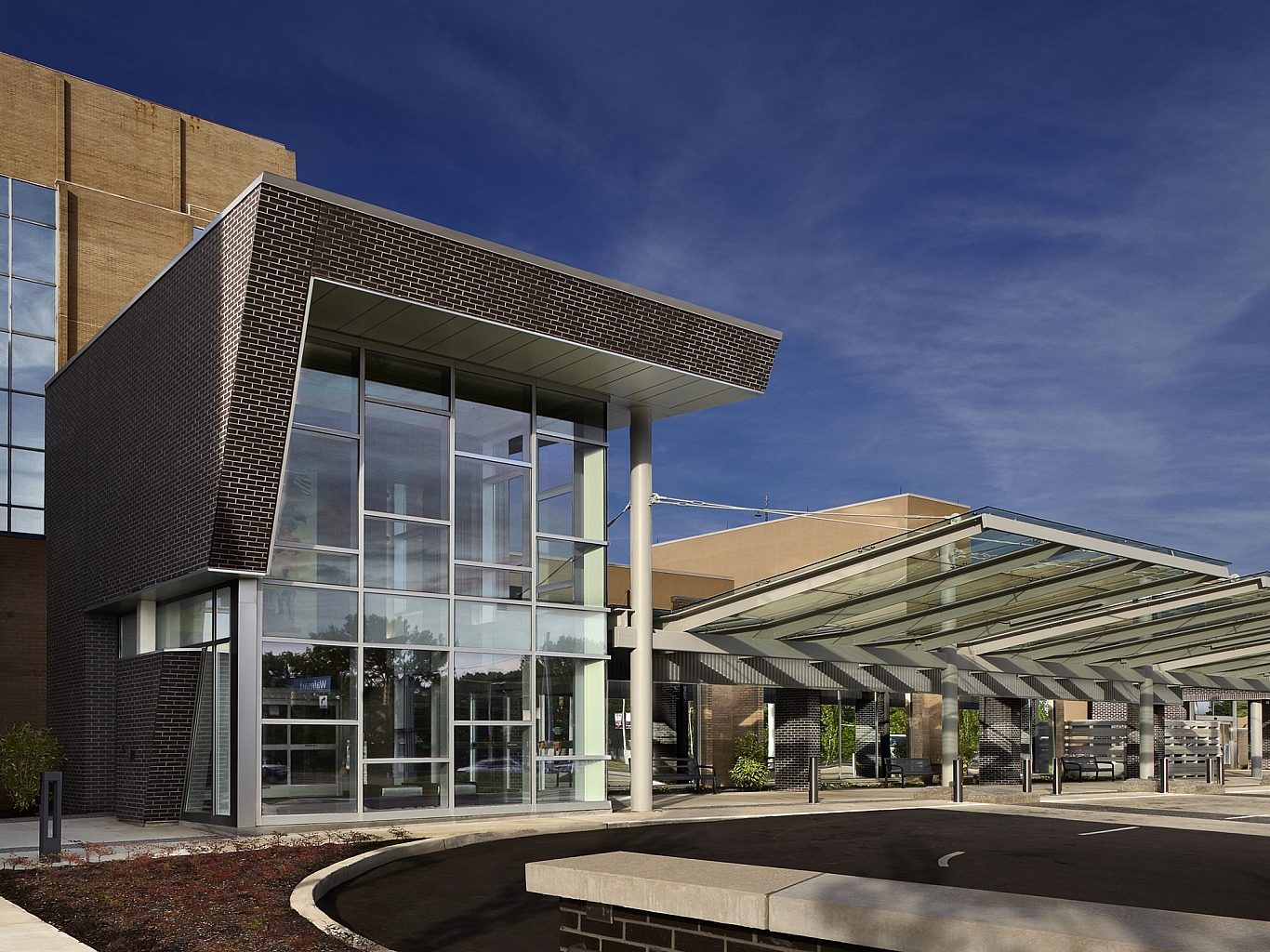 The entrance to a hospital with floor to ceiling windows and a canopy covering the entrance.
