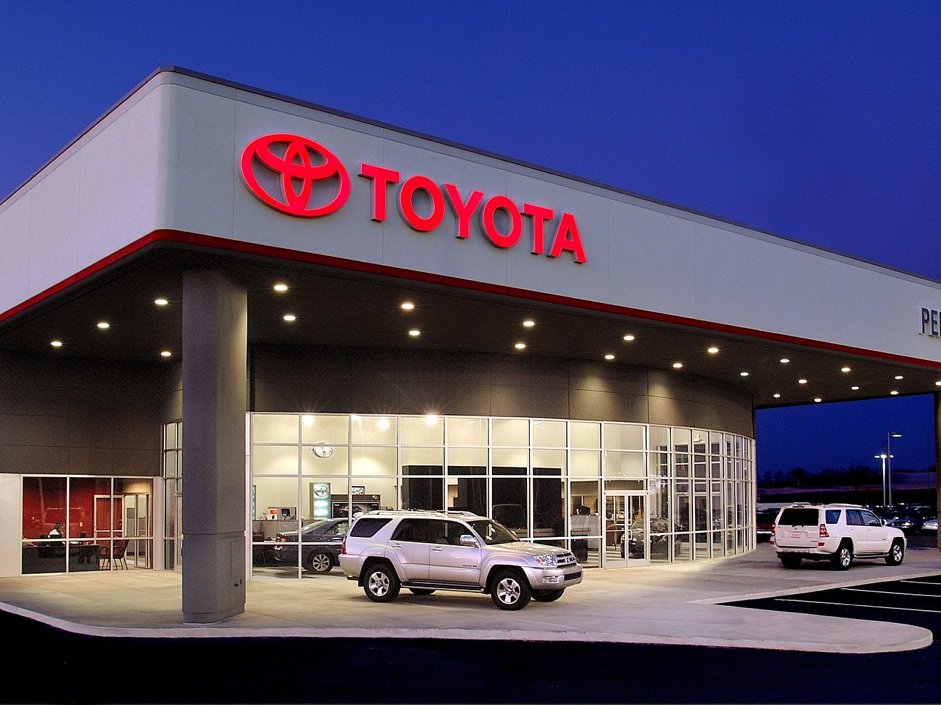 The exterior of a Toyota car dealership with a silver Forerunner sitting on display outside. The Toyota logo is on the front.