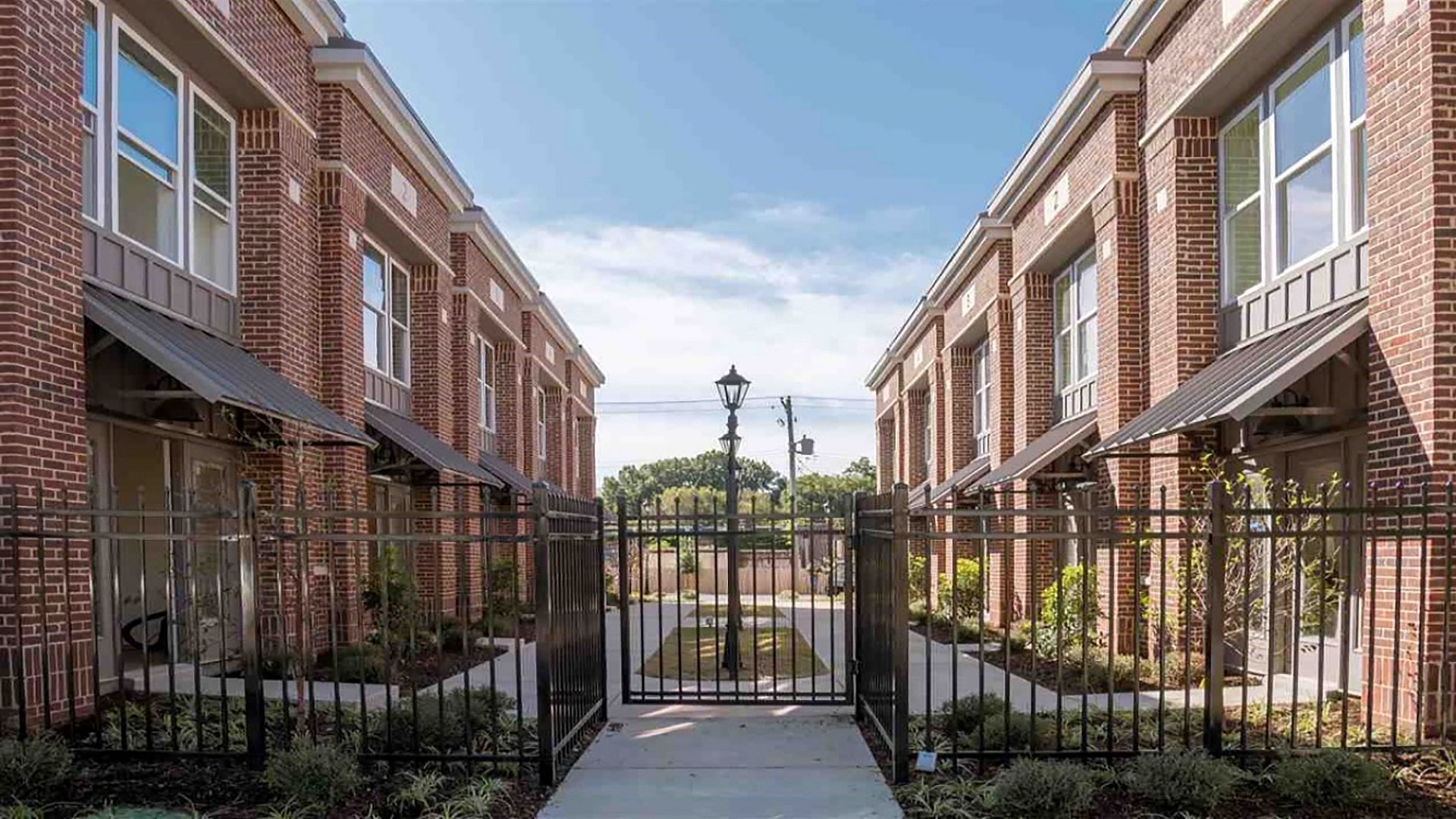 The courtyard of an apartment building with a metal fence blocking it off and street lamps in the middle.