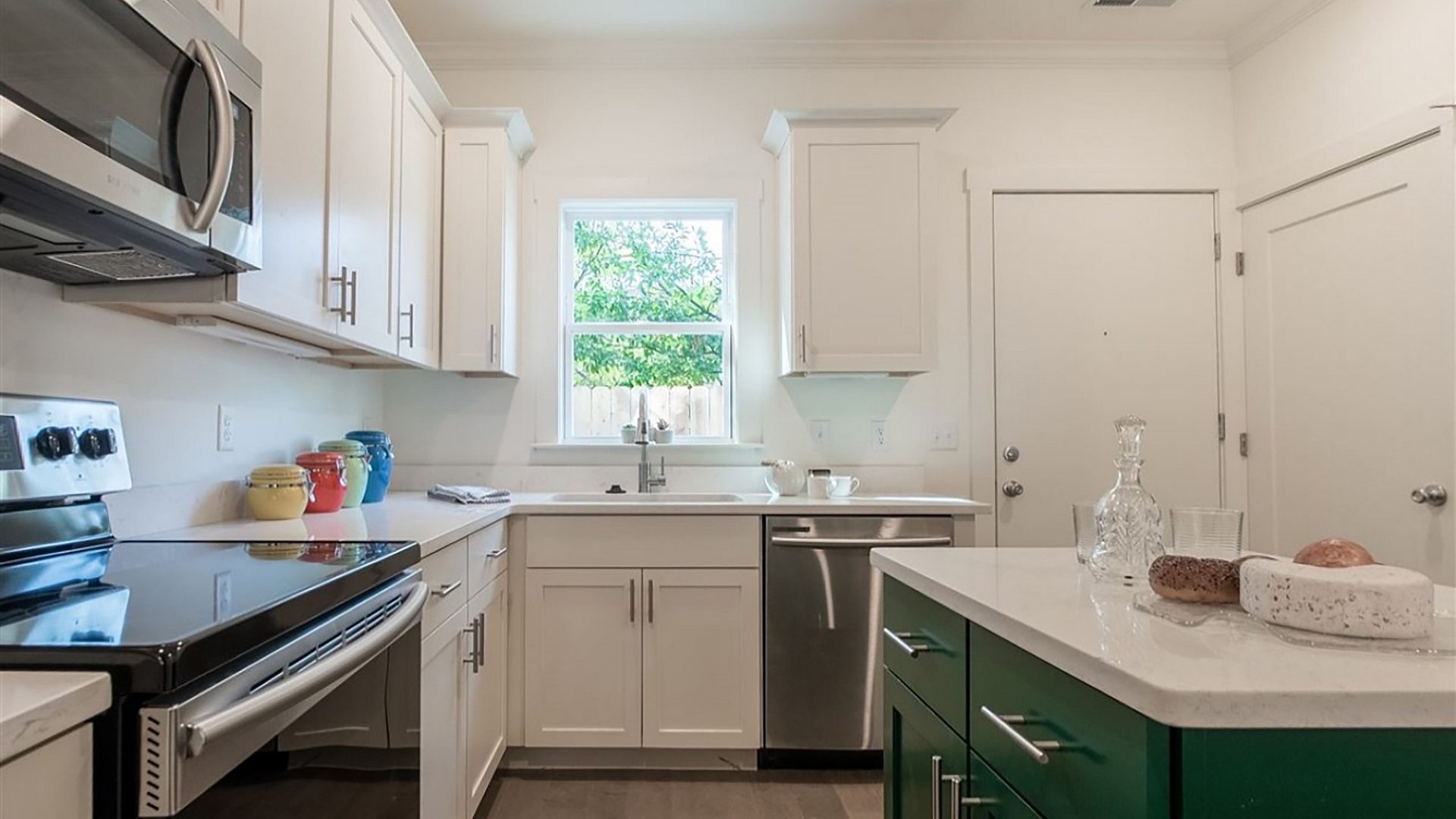 A kitchen in an apartment with an oven and microwave on the left and built in cabinets. A kitchen island is on the right, and a window is above the sink.