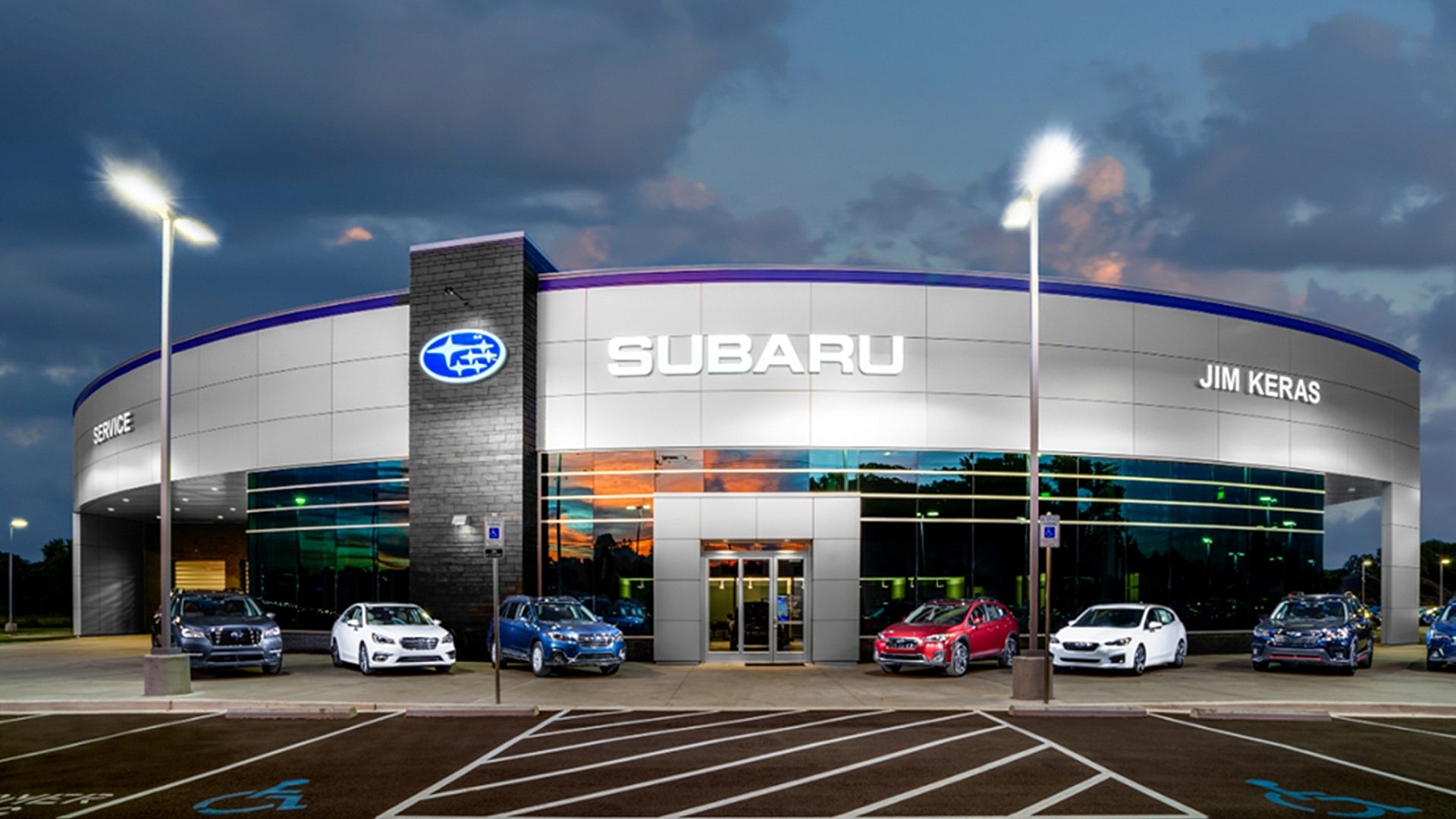 A Subaru dealership lit at night with cars parked on display out front.