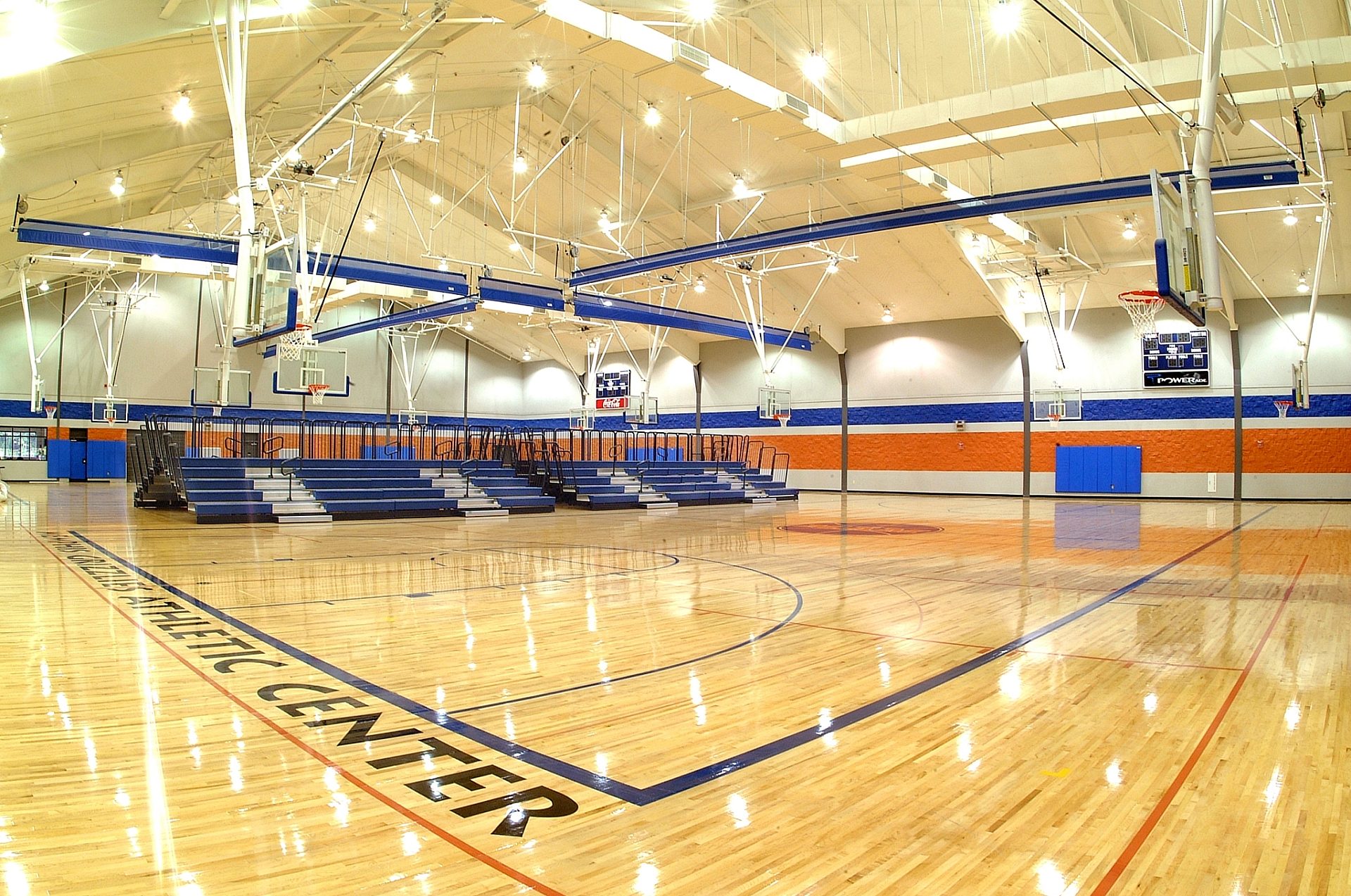 A basketball gym with dark blue bleachers along the far wall. Basketball goals hang from the ceiling, and Grizzlies Athletic Center is written across the floor.