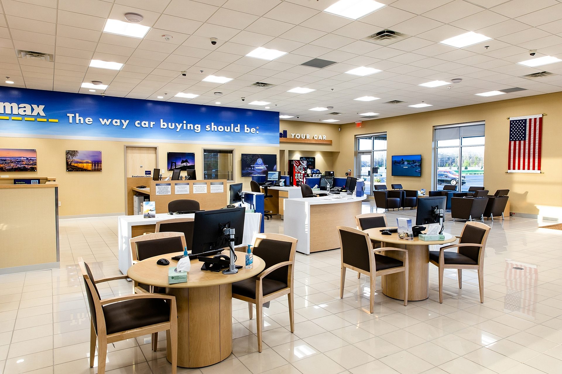 The waiting area of a CarMax dealership with several tables and a few desks.