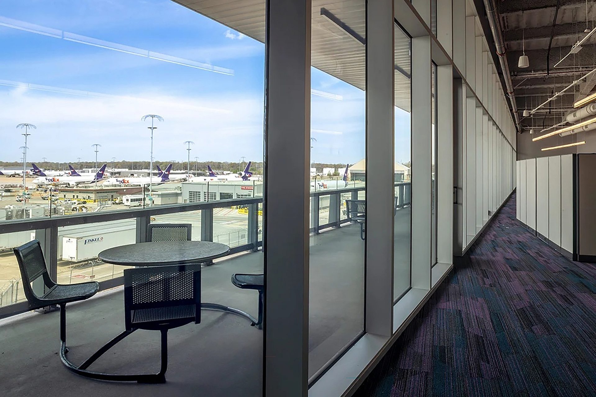 The view of a balcony through floor to ceiling windows. An office cubicle is seen in the background.