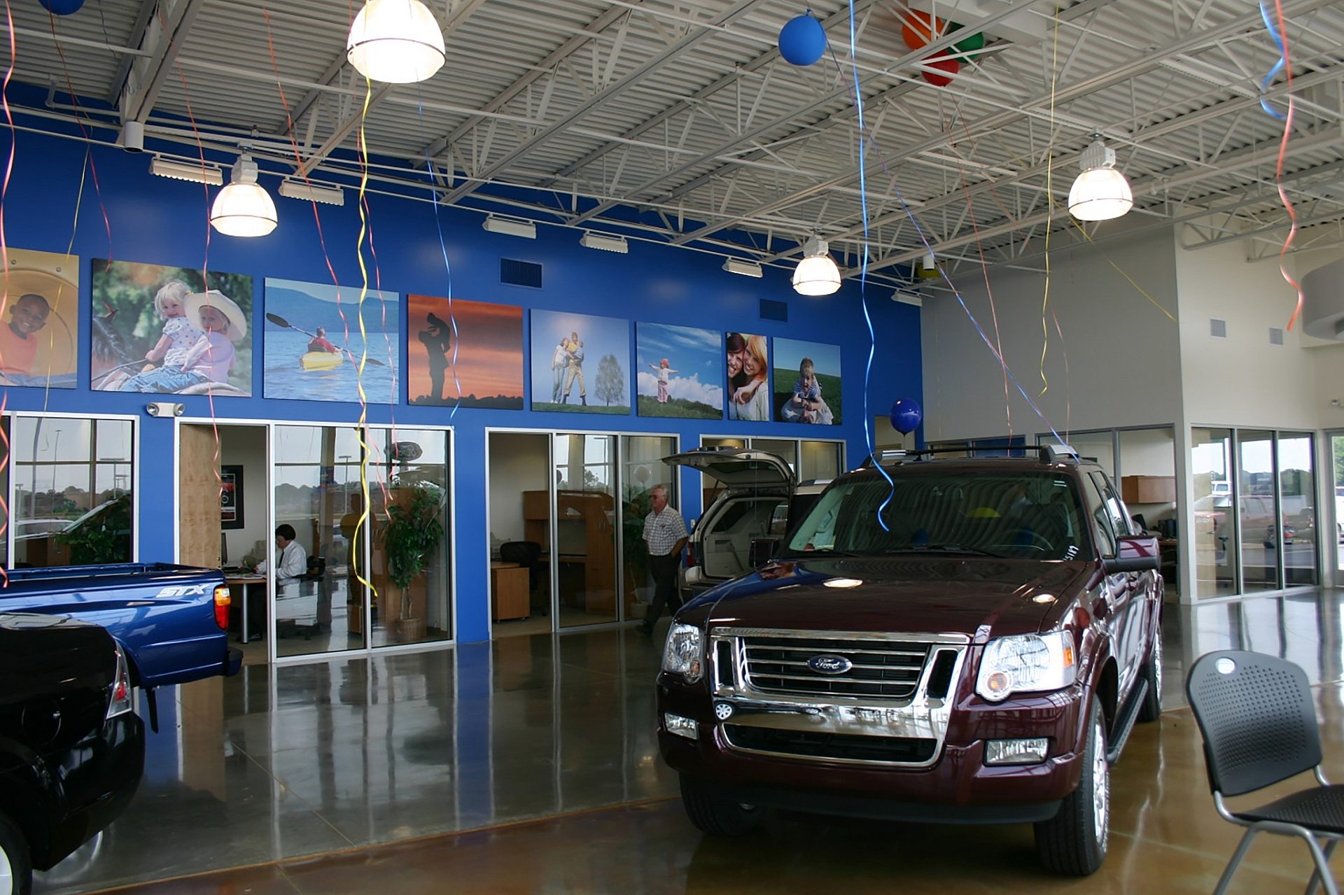 A Ford is parked on display on the inside of the dealership. Offices line the wall behind it.