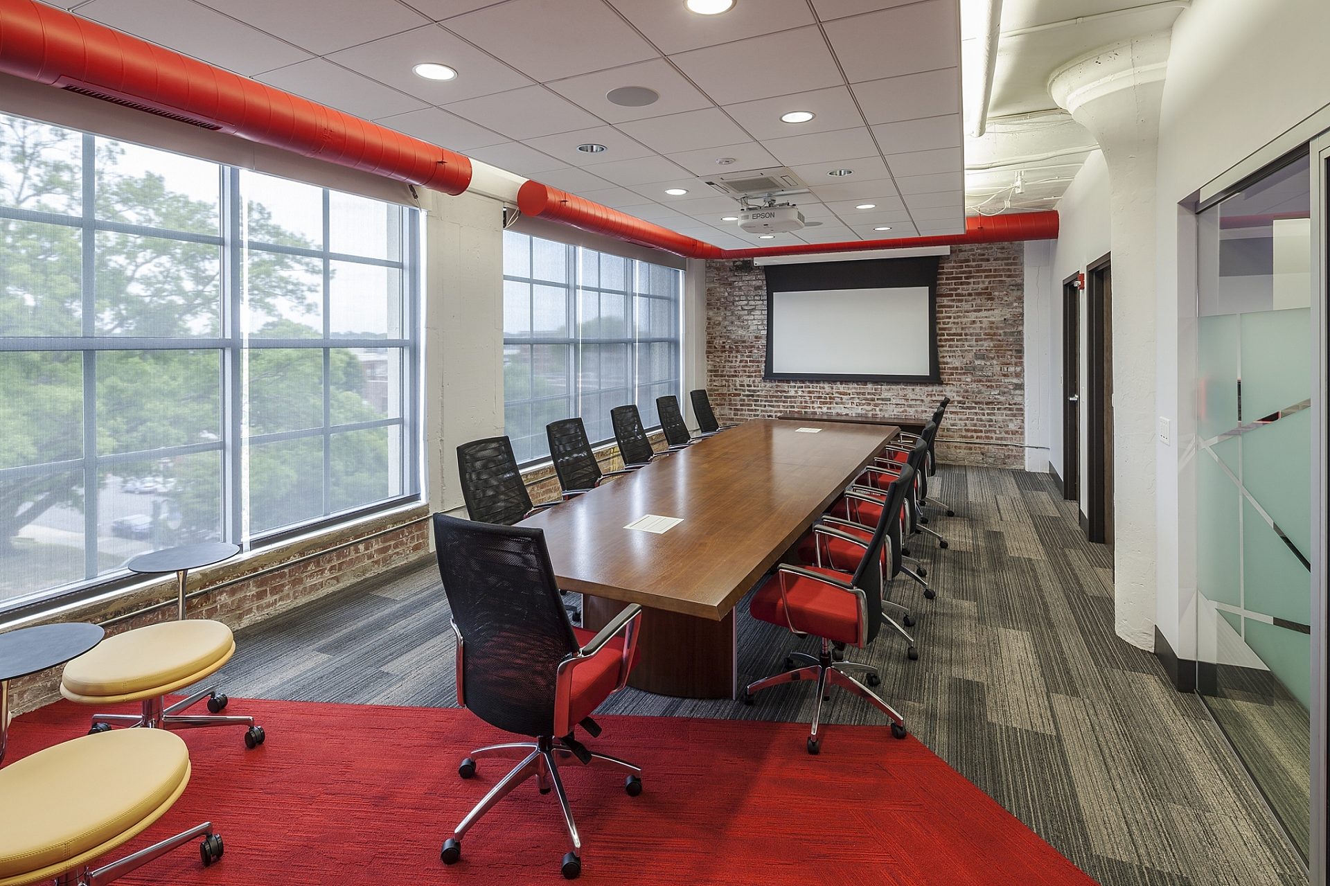 A conference room with a long wooden table down the middle of it and a white projector screen at the end.