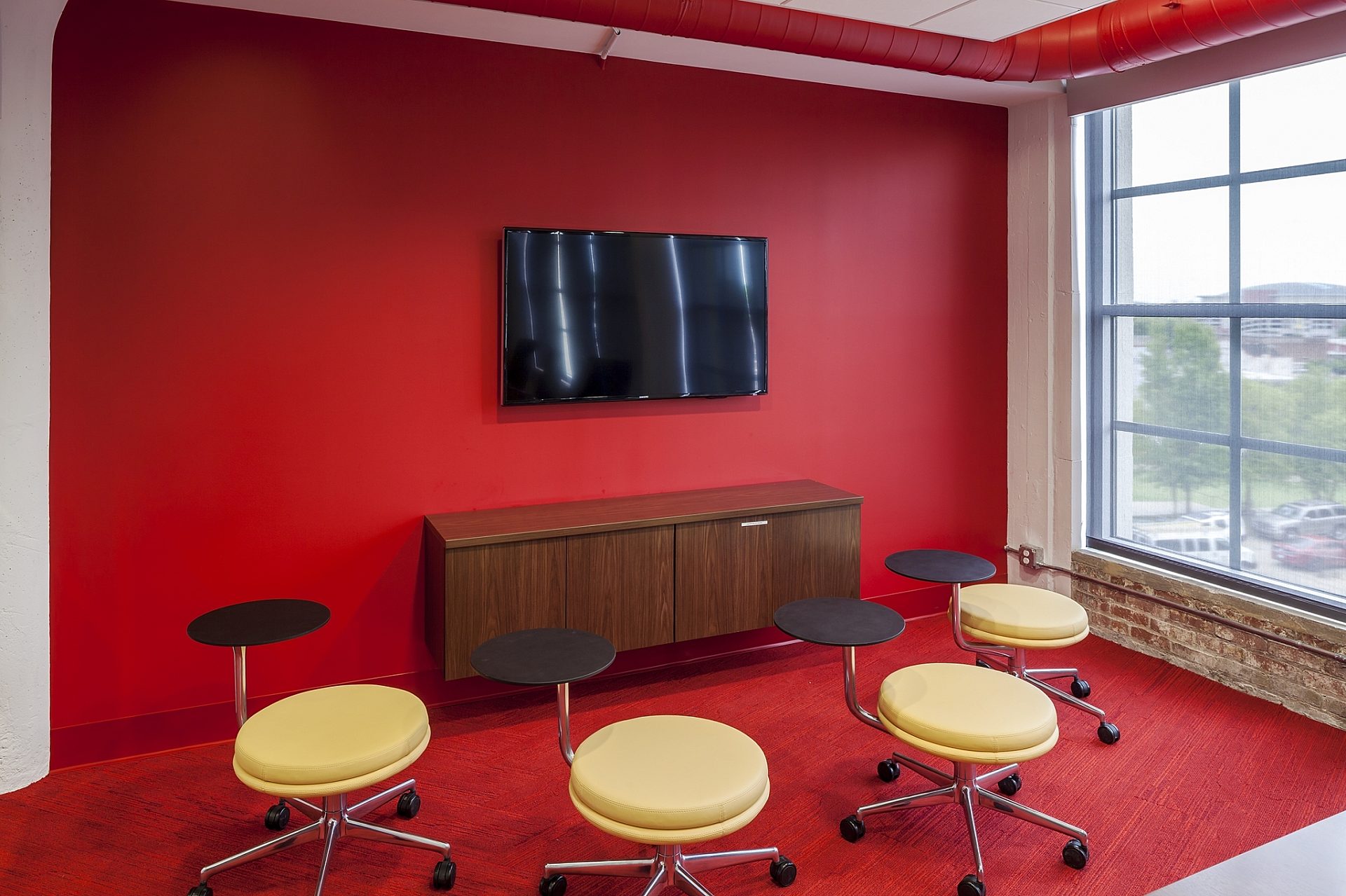 Several rolling stools arranged in a semi-circle face a TV mounted on a wall.