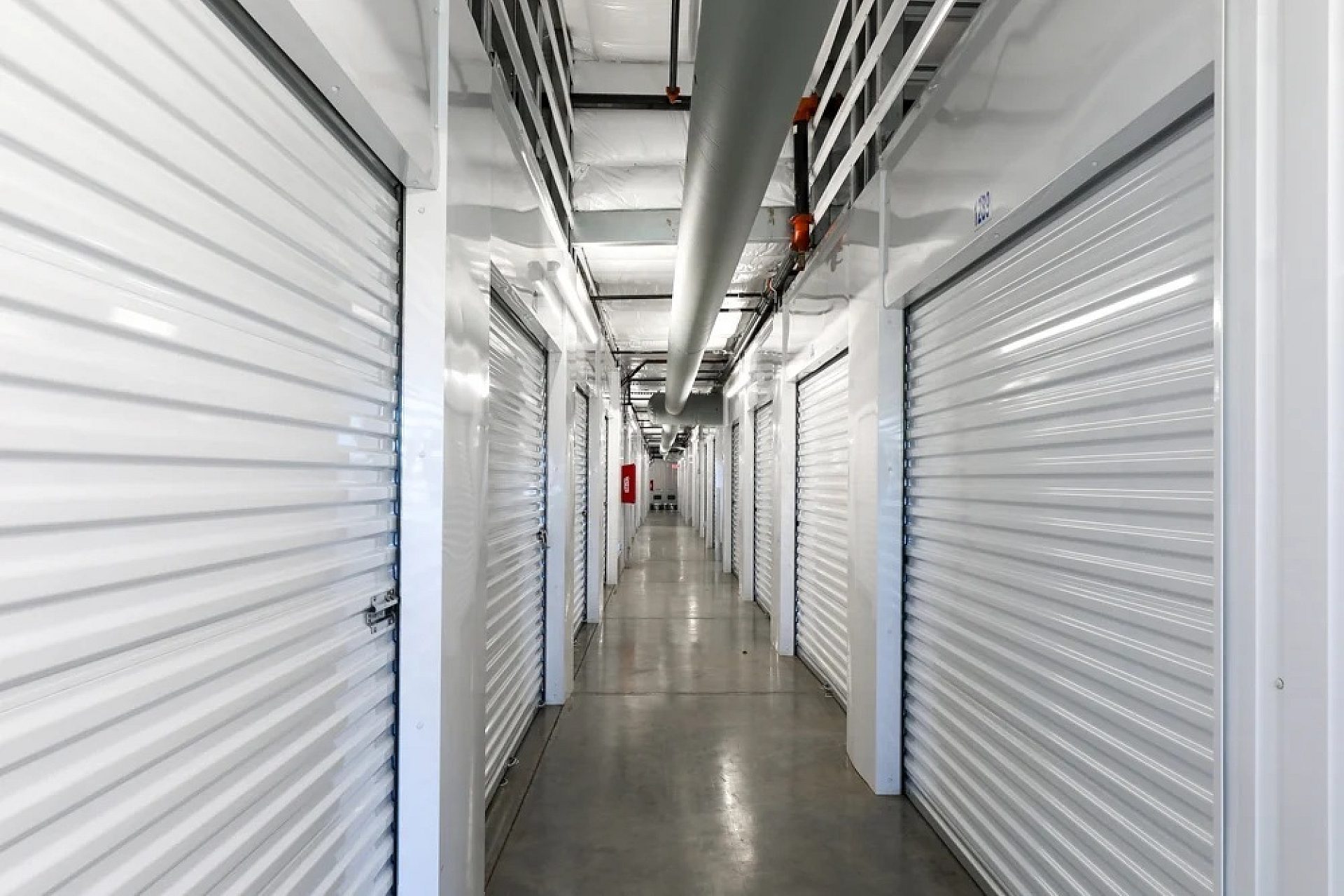 A hallway in a storage facility with white, metalic storage shed doors lining it.