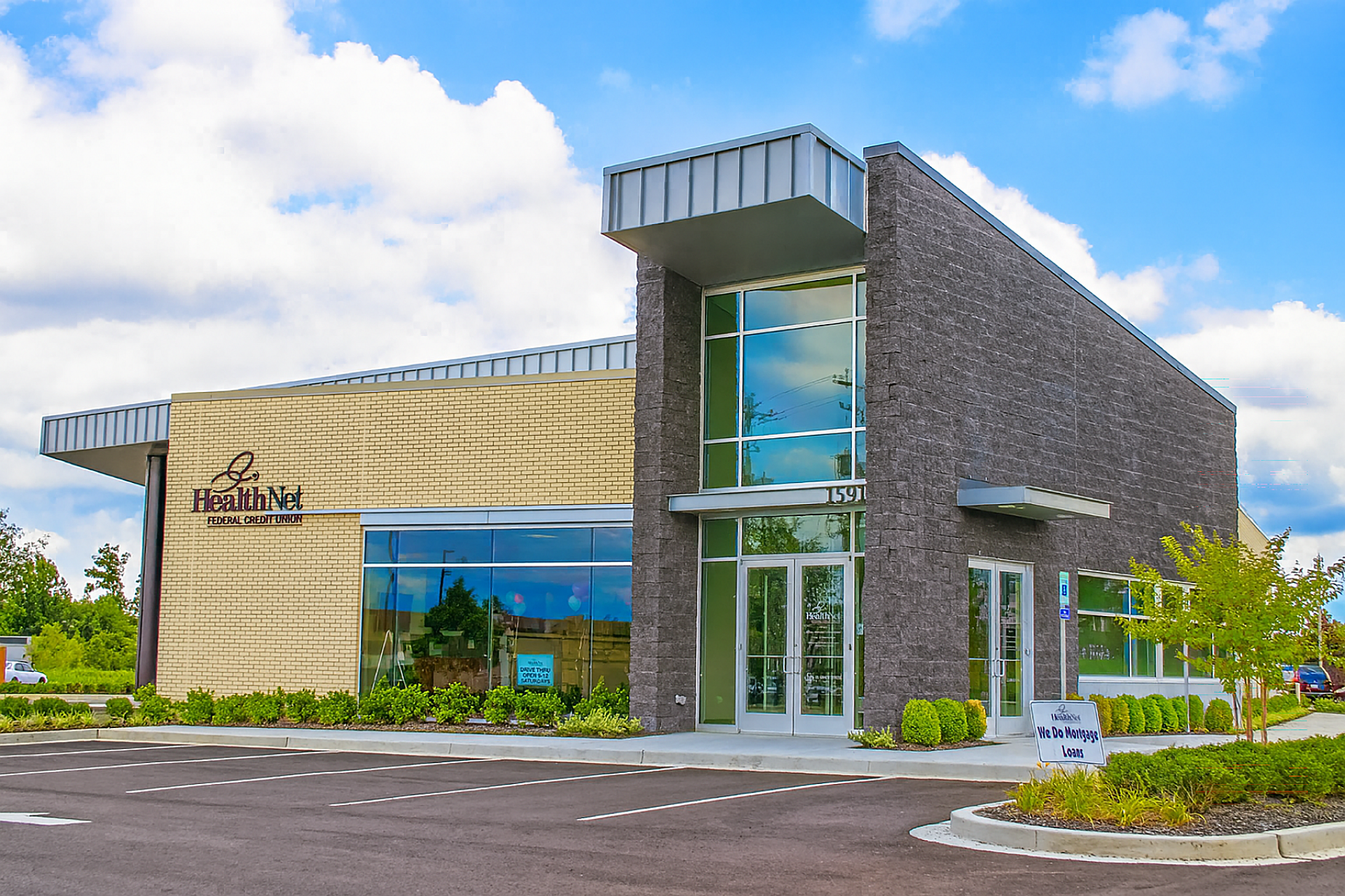 The exterior of an office building for a credit union with wood paneling on one wall and large windows on another portion.