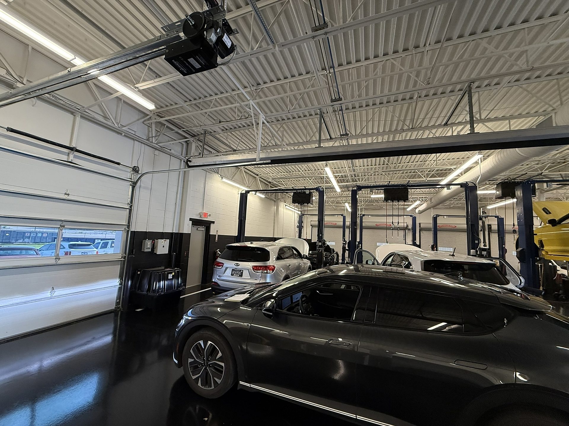 The inside of a mechanic's shop with two cars in the bays and one parked in front of the garage door.