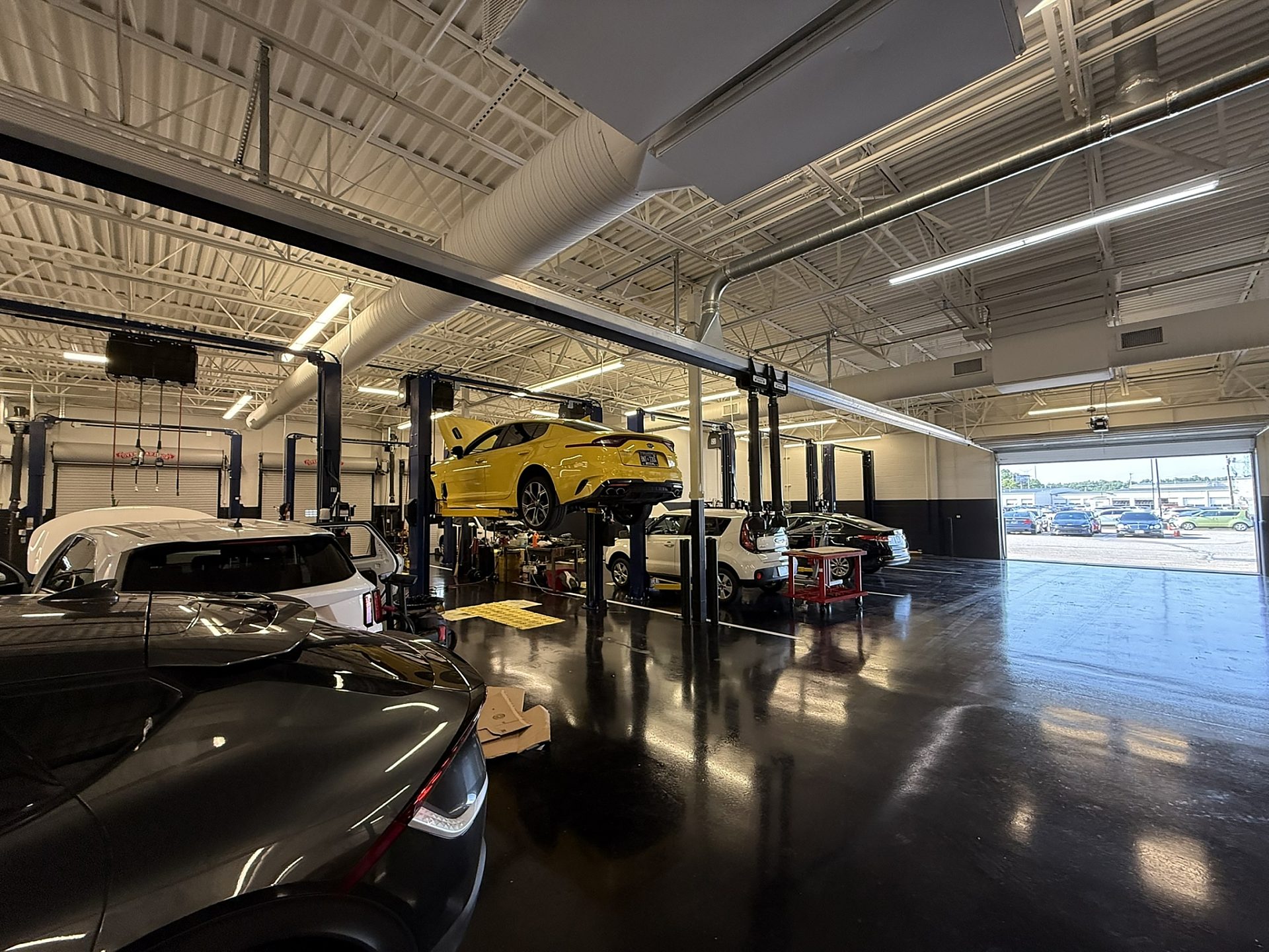 Four bays in an auto mechanic shop with cars in each bay. A yellow car is elevated in the second bay.