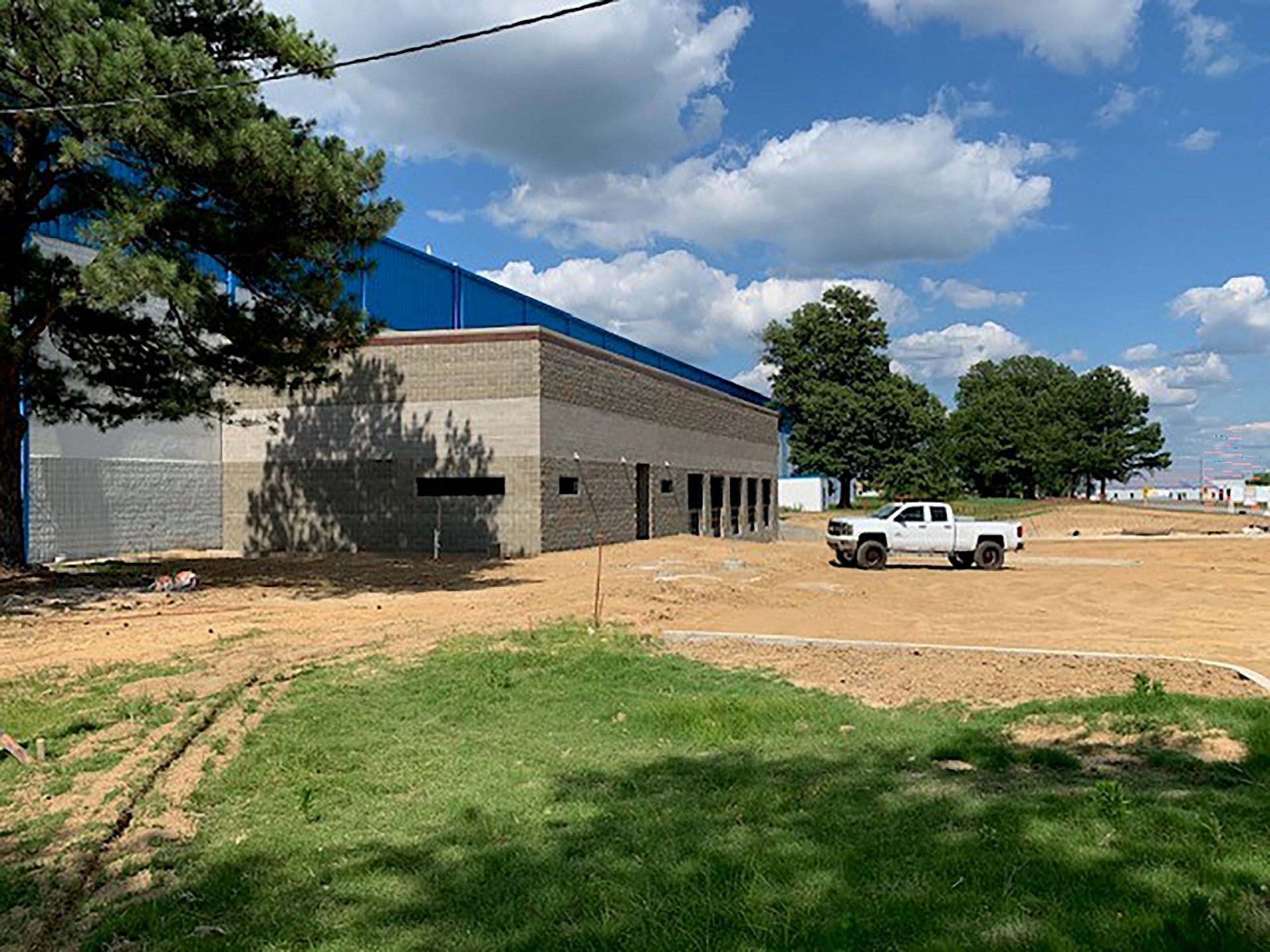 A dirt lot outside of a building under construction with white truck parked in it.