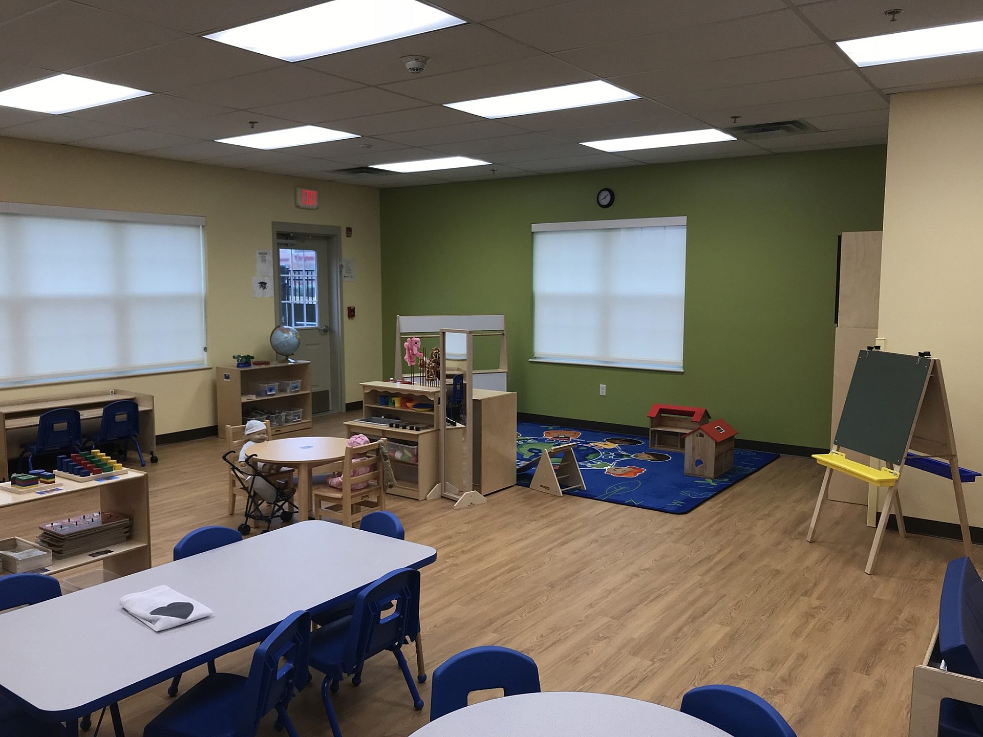 A classroom in a school with tables for desks and an easel in the corner next to a play area.
