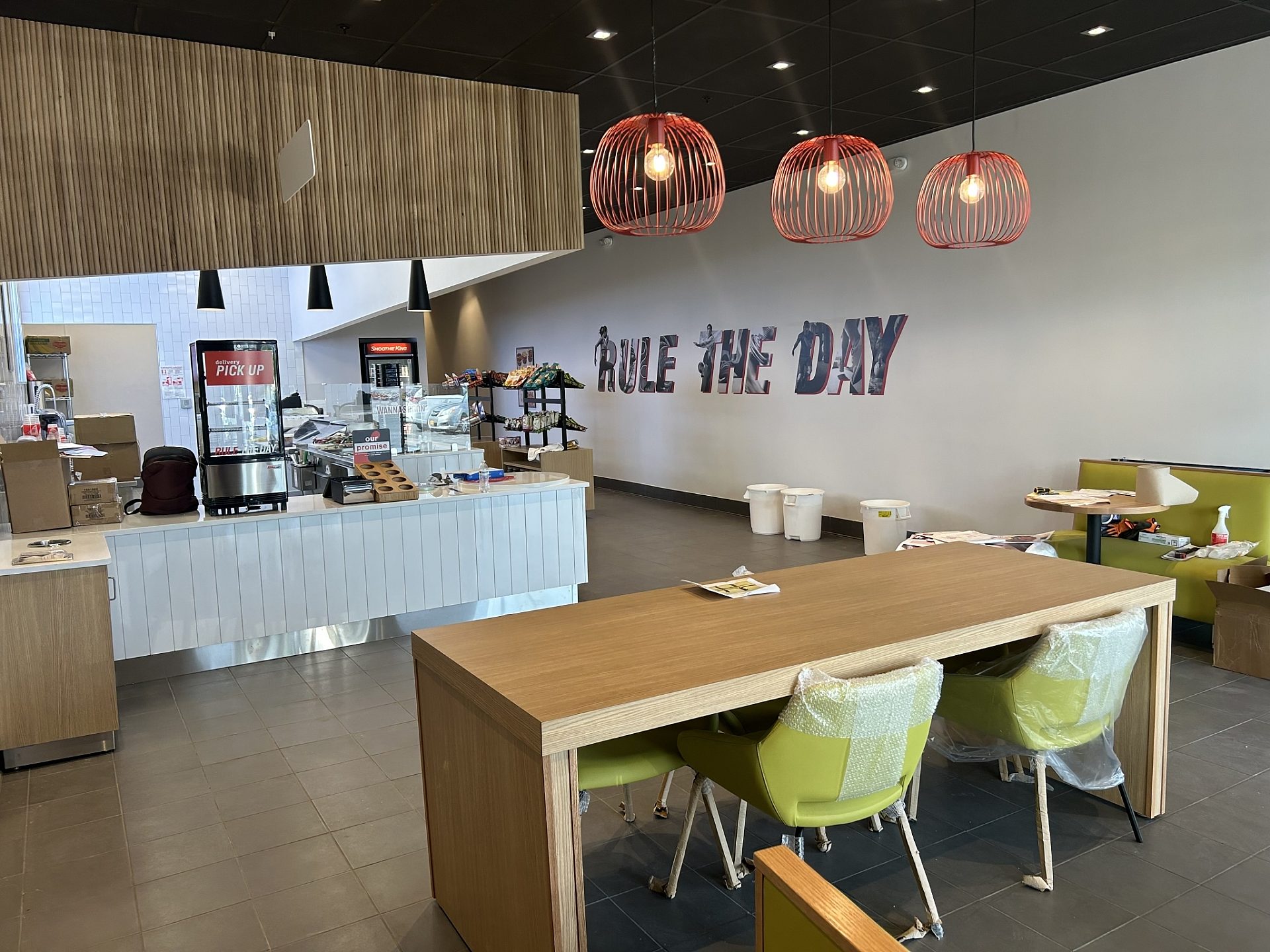 The interior of a smoothie shop under construction facing the register. A wood table and green chairs are in front of it.