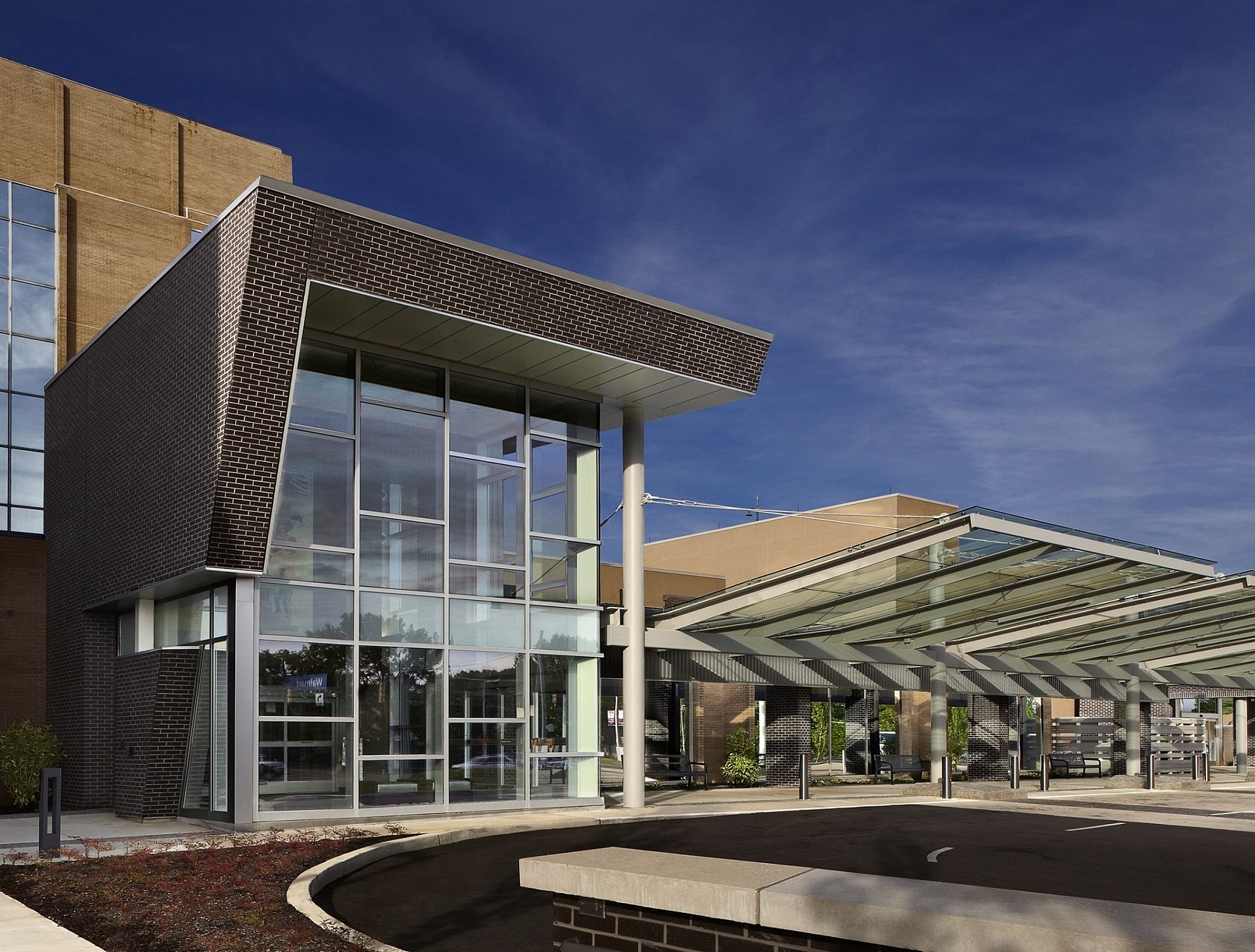 The entrance to a hospital with floor to ceiling windows and a canopy covering the entrance.