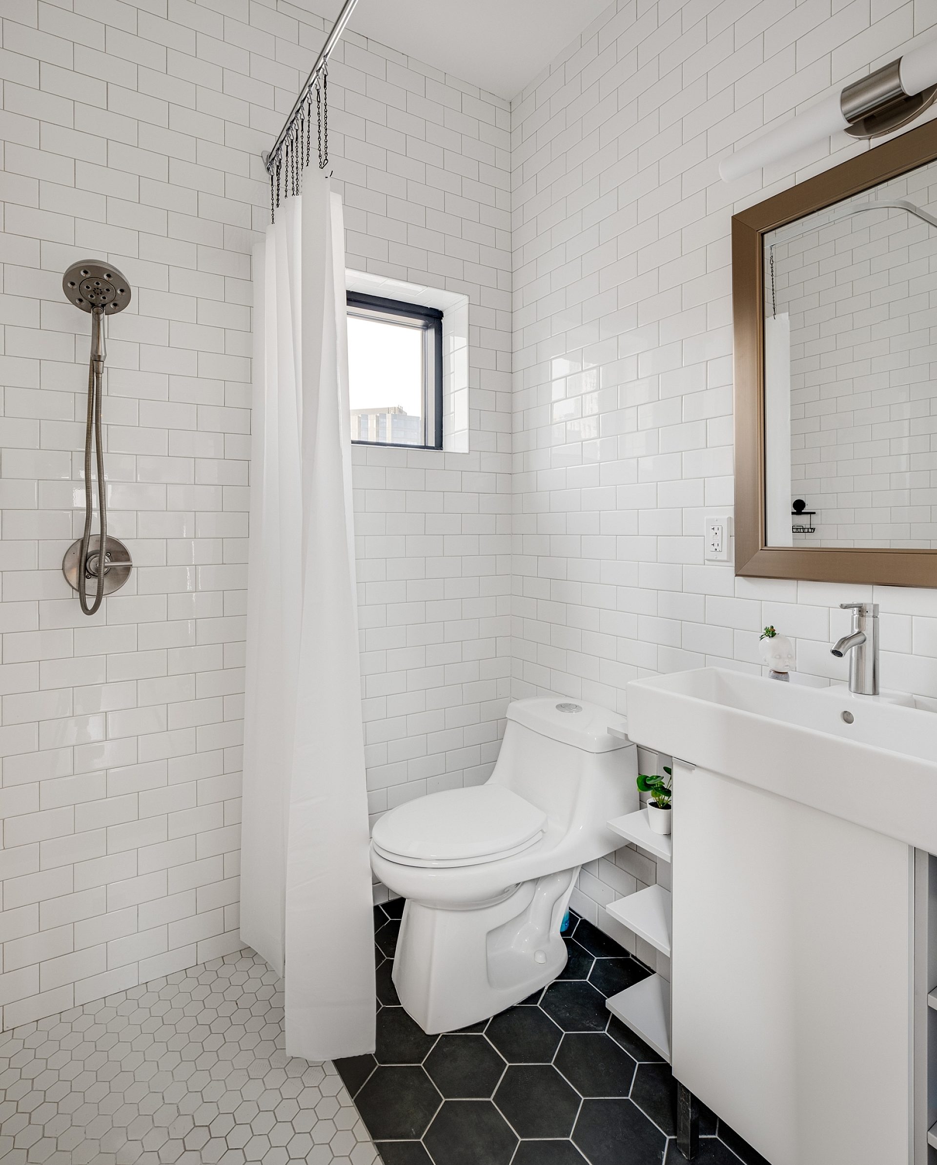 A bathroom with all white tile, featuring a shower, vanity and toilet.
