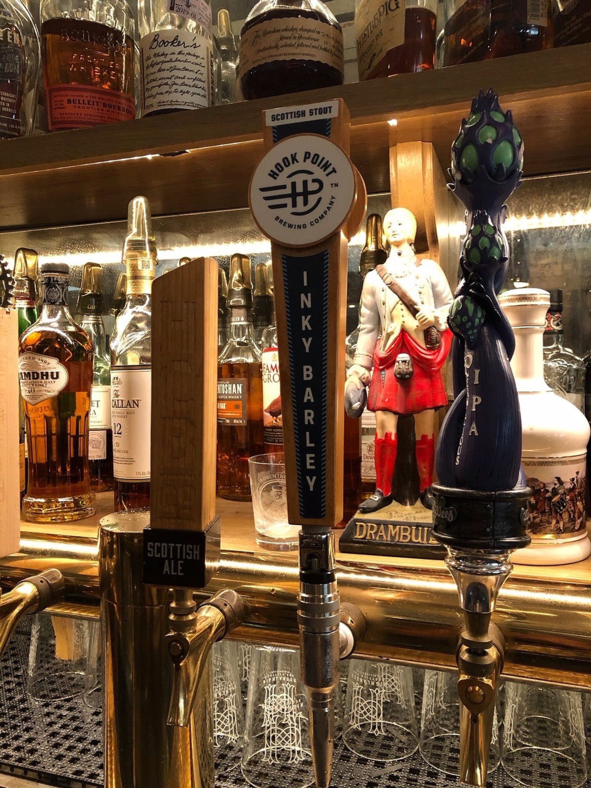 A close up of a beer tap with bottles lining the bar behind it.