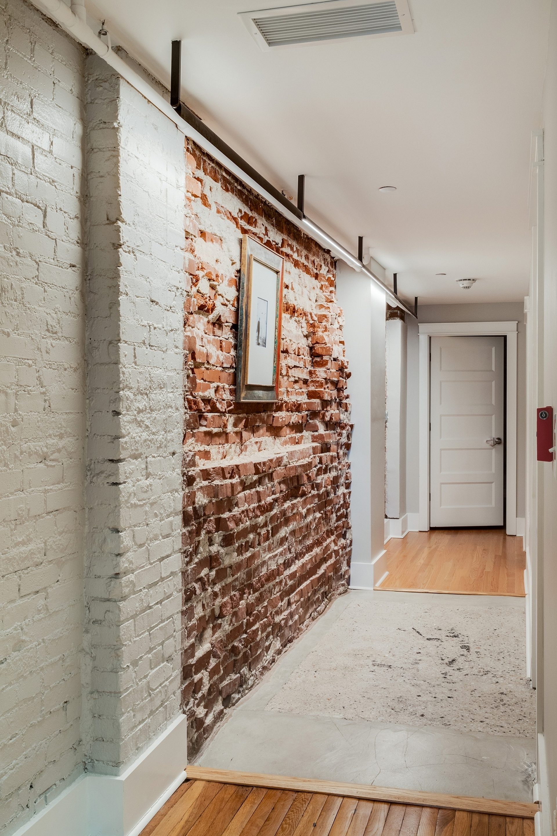Hallway with exposed brick walls leading to another room