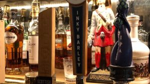 A close up of a beer tap with bottles lining the bar behind it.