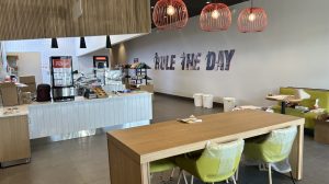 The interior of a smoothie shop under construction facing the register. A wood table and green chairs are in front of it.