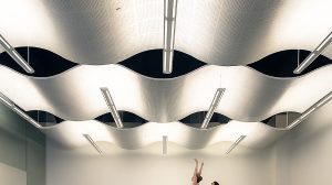 A man and a woman perform a ballet move in a room. A wave-like light fixture hangs from the ceiling, and a ballet bar is on the back wall.