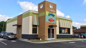 The exterior of a Captain D's restaurant. A red fish is above the entrance, and striped awnings are over the windows. A car is in the drive through.