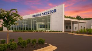 Exterior view of a Ford dealership with Homer Skelton written at the top of the wall. Windows span one side of it.