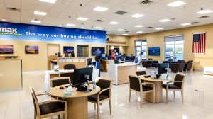 The waiting area of a CarMax dealership with several tables and a few desks.