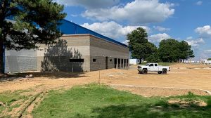 A dirt lot outside of a building under construction with white truck parked in it.
