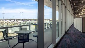 The view of a balcony through floor to ceiling windows. An office cubicle is seen in the background.