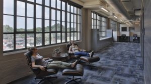 Two people sit in leather chairs in the hallway of a building. Large windows sit on the wall behind them.