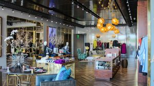 The interior of a clothing store, with a chair and table at the front and a display case on the right side.