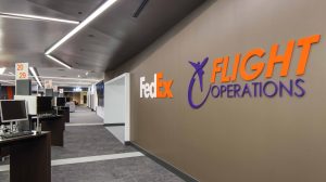 A hallway in a FedEx office building with desks with computers on them lining the left side.
