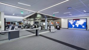 An office space with computers for use on a desk and printing stations on the right. A world map is on one wall.