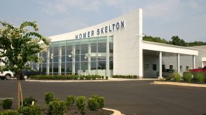 Exterior view of a Ford dealership with full-size windows on one wall. Homer Skelton is seen at the top of the wall.
