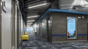 A hallway in an office building with yellow ottomans along the wall and office rooms on the right.