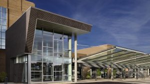 The entrance to a hospital with floor to ceiling windows and a canopy covering the entrance.