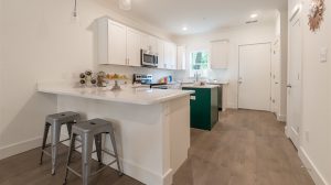 A view of a kitchen from another room, looking over the counter towards the kitchen island. Two metal barstools are under the counter.