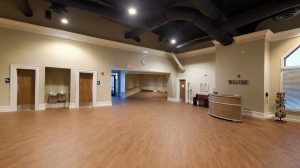 An empty room with two doors on one wall leading to bathrooms, and a larger open door leading to other parts of a church.