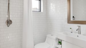 A bathroom with all white tile, featuring a shower, vanity and toilet.