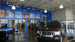 A Ford is parked on display on the inside of the dealership. Offices line the wall behind it.