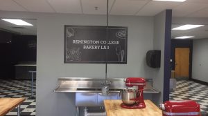 An industrial sink on the back wall of a college culinary classroom. A wooden table has two mixers on it.