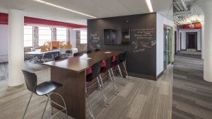 A common space in an office with an island and bar stools around it.