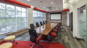A conference room with a long wooden table down the middle of it and a white projector screen at the end.
